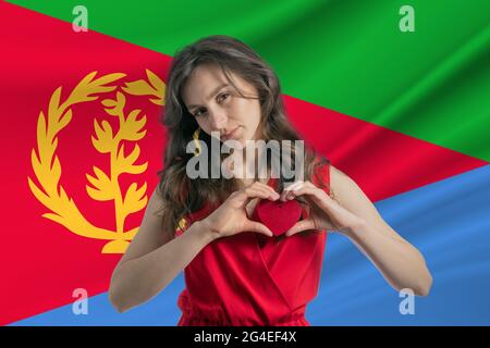 Liebe Eritrea EIN Mädchen hält vor dem Hintergrund der Flagge Eritreas ein Herz auf ihrer Brust in den Händen das Konzept des Patriotismus. Stockfoto