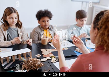 Rückansicht einer Lehrerin, die während des Kunst- und Handwerkskurzens in der Schule Holzmodelle vor einer Gruppe von Kindern vorführt Stockfoto