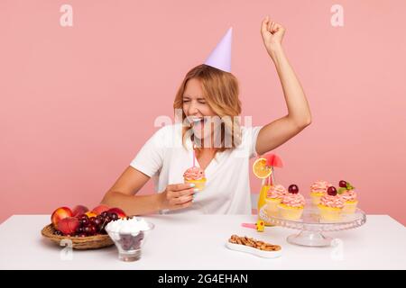 Aufgeregte blonde junge Erwachsene Frau feiert Geburtstag, hält Kuchen mit Kerze, brüllt glücklich, genießen Traum wahr in ihrem Urlaub. Stu Stockfoto