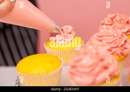 Zugeschnittenes Bild von Muffins oder Kuchen vom Bäcker dekoriert, unbekannte Person Konditor schön Dekoration Desserts, Vorbereitung Gebäck zum Servieren. Indoo Stockfoto