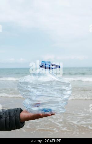 Nahaufnahme eines jungen Mannes mit einer zerdrückten gebrauchten Plastikflasche in der Hand, frisch aus dem Sand eines Strandes gesammelt, als Aktion zur Säuberung der Natura Stockfoto
