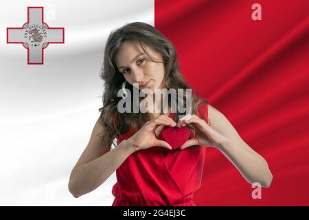 Ich Liebe Malta. Ein Mädchen hält ein Herz auf ihrer Brust in den Händen vor dem Hintergrund der Flagge Maltas. Der Begriff des Patriotismus. Stockfoto