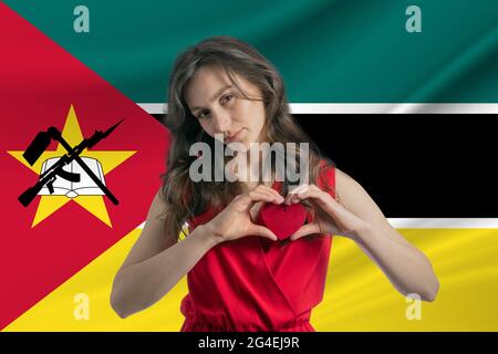 Ich Liebe Mosambik. Ein Mädchen hält vor dem Hintergrund der Flagge Mosambiks ein Herz auf ihrer Brust in den Händen. Der Begriff des Patriotismus. Stockfoto