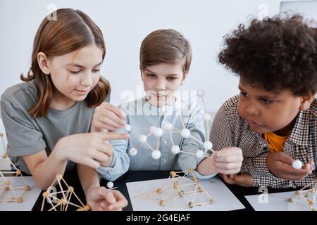 Gruppe von drei Kindern, die während des Kunst- und Handwerkskurzens in der Schule mit Holzmodellen spielen Stockfoto