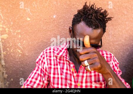 MBOUR, SENEGAL - JANUAR CIRCA, 2021. Nicht identifizierter senegalesischer, ziemlich reifer Mann in traditioneller Kleidung im Freien, der lächelnd aufschaut. Armut und Glück Stockfoto