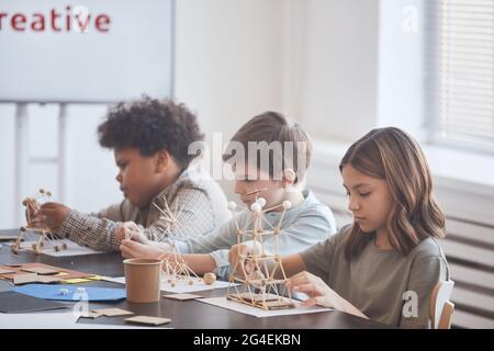 Gruppe von Schulkindern, die in Reihe sitzen und Holzmodelle machen, während sie in der Schule Kunst- und Handwerkskurs genießen Stockfoto