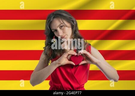 Ich Liebe Catalonia. Ein Mädchen hält vor dem Hintergrund der katalanischen Flagge ein Herz auf ihrer Brust in den Händen. Der Begriff des Patriotismus. Stockfoto