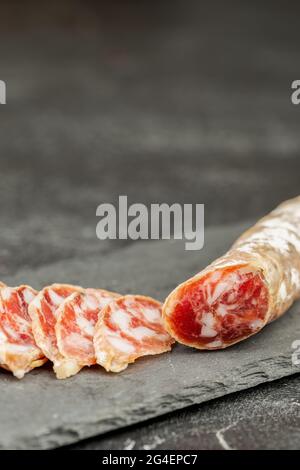 Traditionelle rauchgetrocknete Schweinewurst auf einer Schiefertafel über dunklem Hintergrund. Platz für Text Stockfoto