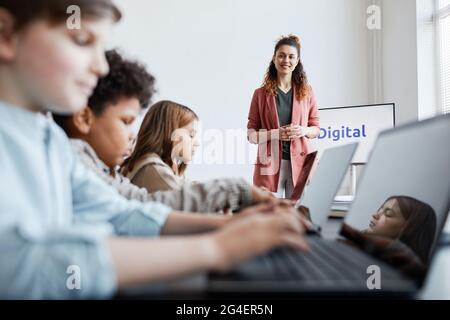 Porträt einer lächelnden Lehrerin mit einer Gruppe von Kindern, die während DES IT-Unterrichts in der Schule Computer benutzen Stockfoto