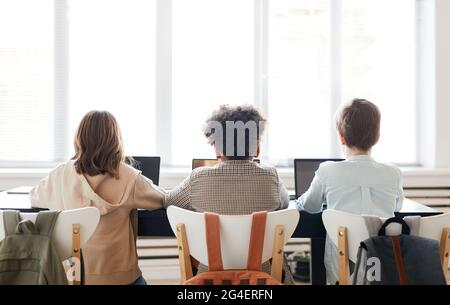 Rückansicht einer Gruppe von drei Kindern, die während des IT-Unterrichts in der Schule in Reihe sitzen und Computer benutzen, Platz kopieren Stockfoto