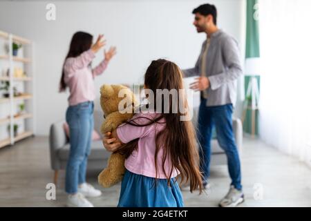 Familienstreitigkeiten Konzept. Kleines Mädchen, das unter Familienstreitigkeiten leidet, ihren Teddybär kuschelt und sich den Eltern zuwendet Stockfoto