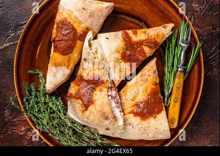 Calzone Pizzateile auf rustikalem Teller mit Tomatensauce und Kräutern. Dunkler Hintergrund. Draufsicht Stockfoto