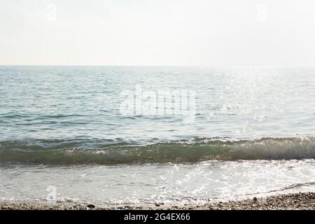 Silbernes Meer glitzernden Hintergrund. Minimalistische Sommerlandschaft in Grau- und Silbertönen. Mittags heißer Tag. Die helle Sonne spiegelt sich in den Wellen wider Stockfoto