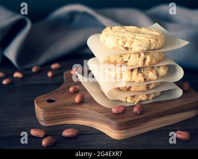 Haufen Erdnusskekse auf einem Holzbrett, dunkler rustikaler Hintergrund. Hausgemachte Nuss-Kekse auf weißem Papier für Gebäck Stockfoto