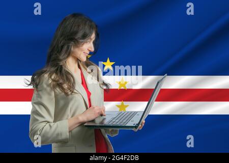 Freiberuflerin auf den Kapverden die schöne junge Freiberuflerin nutzt einen Laptop vor dem Hintergrund der Flagge Kapverdes. Stockfoto