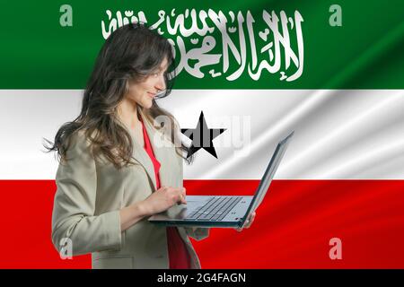 Freiberuflich in Somaliland. Schöne junge freiberufliche Frau nutzt Laptop-Computer vor dem Hintergrund der Flagge von Somaliland. Stockfoto