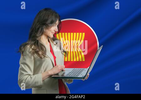 Freiberuflich in Association of Southeast Asian Nations. Schöne junge freiberufliche Frau nutzt Laptop-Computer vor dem Hintergrund der Flagge von Assoc Stockfoto