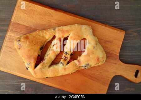 Draufsicht auf ein Fougasse französisches Fladenbrot mit sonnengetrockneter Tomate und Olive auf Holzhintergrund Stockfoto