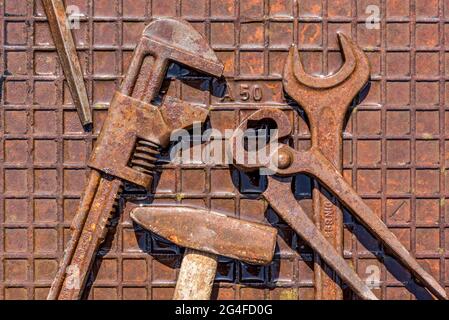 Altes Werkzeug mit Engländer, Hammer, Biss Zange, Schraubenschlüssel auf nasser rostiger Eisenplatte, Deutschland Stockfoto