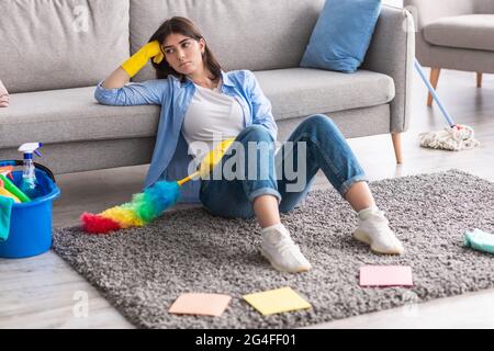 Aufgeregte Frau, die es leid war, auf dem Teppich zu sitzen und zu putzen Stockfoto