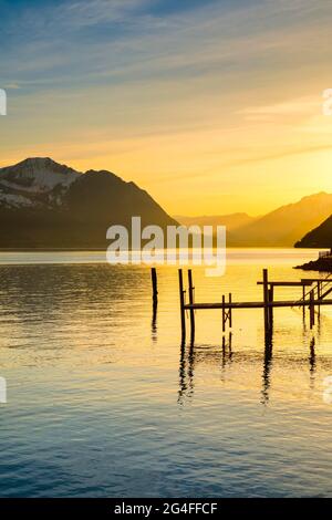 See mit Bergen im Hintergrund, Blick vom Brunnen über den Vierwaldstättersee bei Sonnenuntergang mit Steg im Vordergrund, Kanton Schwyz, Schweiz Stockfoto