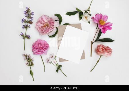 Geblümter Sommer-Schreibwaren-Mockup. Leere Grußkarte mit Umschlag. Gartenblumen und Kräuter isoliert auf weißem Tischhintergrund im Sonnenlicht. Rosen Stockfoto