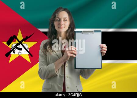 Studieren Sie in Mosambik. Schöne Frau, die ein Blatt Papier in den Händen hält. Mädchen auf dem Hintergrund der Flagge von Mosambik. Stockfoto