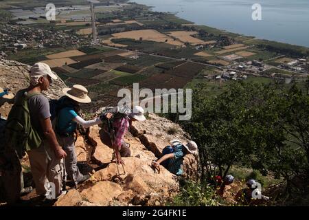 Wanderer, ältere Erwachsene in den 50er und 60er Jahren, wandern einen steilen Abstieg auf Felsen vom Mt. Arbel, darunter der See von Galilee und das historische Magdala. Stockfoto