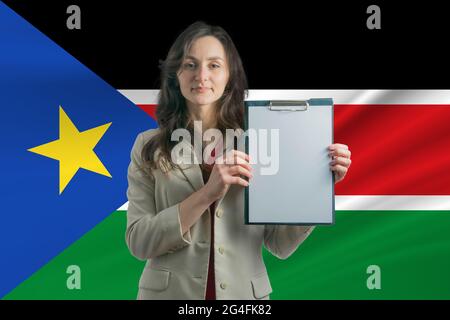 Studieren Sie im Südsudan. Schöne Frau, die ein Blatt Papier in den Händen hält. Mädchen auf dem Hintergrund der Flagge des Südsudan. Stockfoto