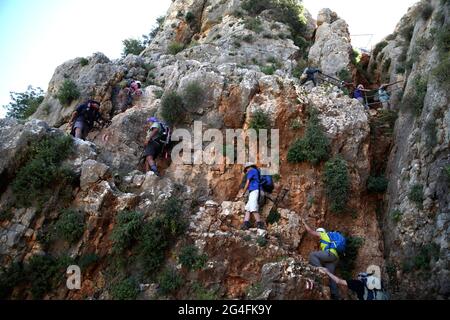 Wanderer, ältere Erwachsene in den 50er, 60er und 70er Jahren, aktive Senioren, benutzen Handgriffe und ein Stahlseil, um einen Felsen hinauf zum Mount Arbel über dem Meer von Galelee zu gehen Stockfoto