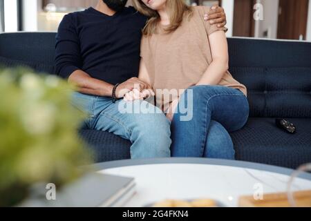 Ein junges verliebter Mann sitzt auf dem Sofa, umarmt und hält die Hände Stockfoto
