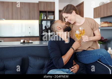 Freund und Freundin verbringen den Abend zu Hause, trinken Wein, schauen sich an und küssen sich fast Stockfoto