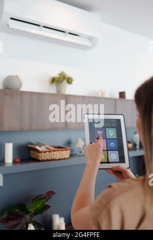 Junge Frau verwendet die Smartphone-Home-Anwendung auf einem Tablet-Computer, wenn sie die Temperatur in ihrer Wohnung eingestellt hat Stockfoto