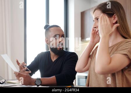 Schockiert emotionalen Mann mit Rechnung in der Hand Blick auf Frau, die die monatliche Hypothek Zahlung zu zahlen vergessen Stockfoto
