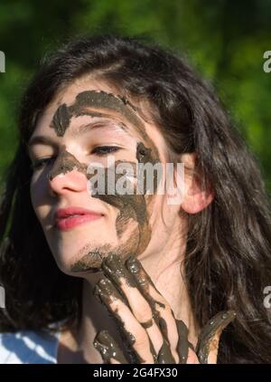 Schlammiges Gesicht einer jungen langhaarigen brünette kaukasischen Frau im Freien an einem sonnigen Sommertag Stockfoto