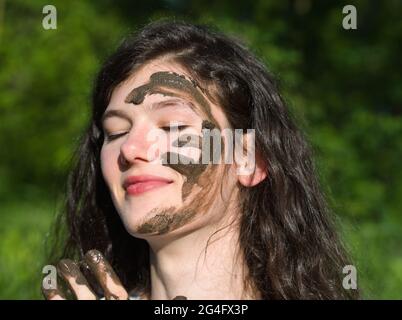 Schlammiges Gesicht einer jungen langhaarigen brünette kaukasischen Frau im Freien an einem sonnigen Sommertag Stockfoto
