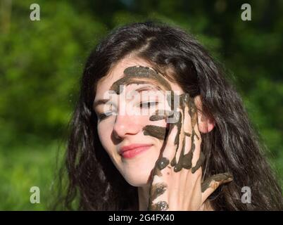 Schlammiges Gesicht einer jungen langhaarigen brünette kaukasischen Frau im Freien an einem sonnigen Sommertag Stockfoto