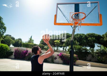 Männlicher Sportler, der Basketball spielt und den Ball auf dem Spielplatz wirft, Blick von hinten. Präzisionsschuss Stockfoto