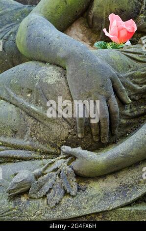 Trauerstatue der Mutter und des sterbenden Kindes, Nahaufnahme mit Händen und rosa Blume Stockfoto