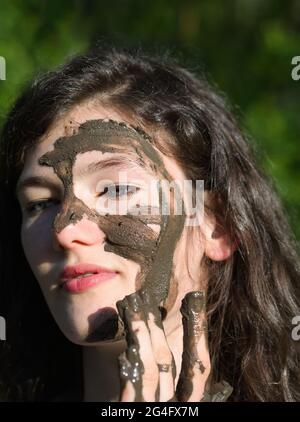 Schlammiges Gesicht einer jungen langhaarigen brünette kaukasischen Frau im Freien an einem sonnigen Sommertag Stockfoto