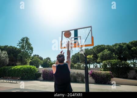 Männlicher Sportler, der Basketball spielt und den Ball auf dem Spielplatz wirft, Blick von hinten Stockfoto