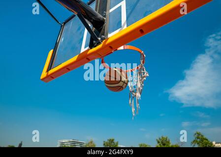 Basketballball fällt durch altes Netz. Auf Spielplatz Blauer Himmel auf Hintergrund Stockfoto