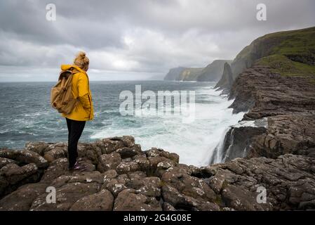 Eine Frau, die das Meer entlang des Traelanipa Wanderweges am See Sorvagsvatn auf der Insel Vagar auf den Färöer Inseln betrachtet Stockfoto