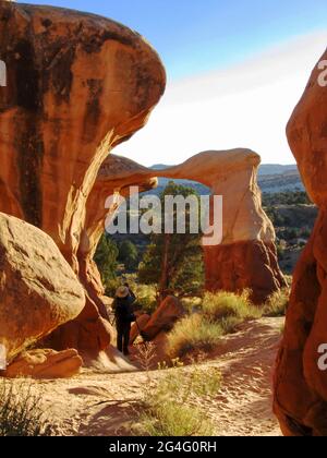 Ein Fotograf, der am späten Nachmittag den Metate Arch fotografiert, einen dünnen, feinen Steinbogen im Devils Garden, Escalante, Utah, USA Stockfoto