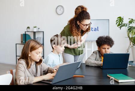 Verschiedene Gruppen von Kindern, die während DES IT-Unterrichts in der Schule mit einer jungen Lehrerin Computer benutzen Stockfoto