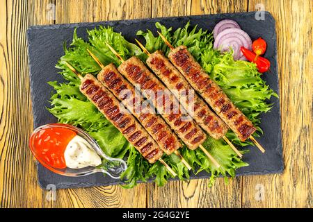 Chevaptschichi, Fleischvorspeise mit Sauce auf einem Steinbrett. Salatblätter und Paprika ergänzen die Fleischplatte. Lula-Kebab. Selektiver Fokus. Stockfoto