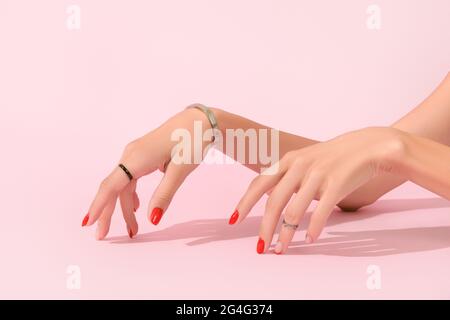 Frauenhand mit roter Maniküre auf rosa Hintergrund. Trends im Maniküre-Design Stockfoto