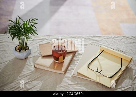 Tasse Tee, Planer, Gläser und Pflanzen in Topf auf Tisch mit zerknitterter Tischdecke bedeckt Stockfoto