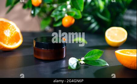Nahaufnahme einer feuchtigkeitsspendenden Gesichtscreme mit natürlichem ätherischem Zitrusöl und Mandarinenbaum, Orange- und Zitronenfrüchten im Hintergrund. Mockup für die Hautpflege Stockfoto