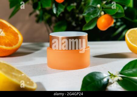 Nahaufnahme eines geschlossenen Glases feuchtigkeitsspendender Gesichtscreme mit natürlichem ätherischem Zitrusöl und Mandarinenbaum sowie Hintergrund von Orangen- und Zitronenfrüchten. Modell für Stockfoto